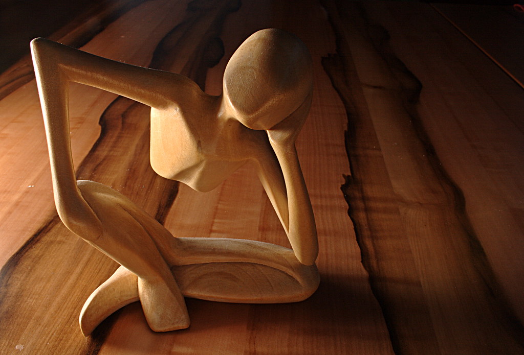 A wooden sculpture in a thinking position on the floor.