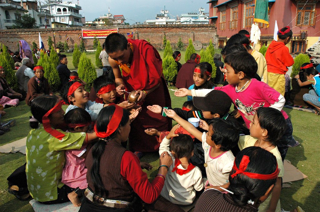 buddhist monk standing, encircled by children receiving nectar from the monk.