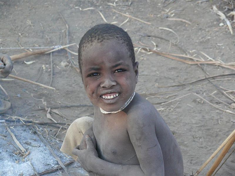 young boy of color covered in ash sitting in the desert.
