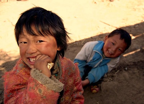 small child using their mouth to open a food wrapper while another child smiles in the background.