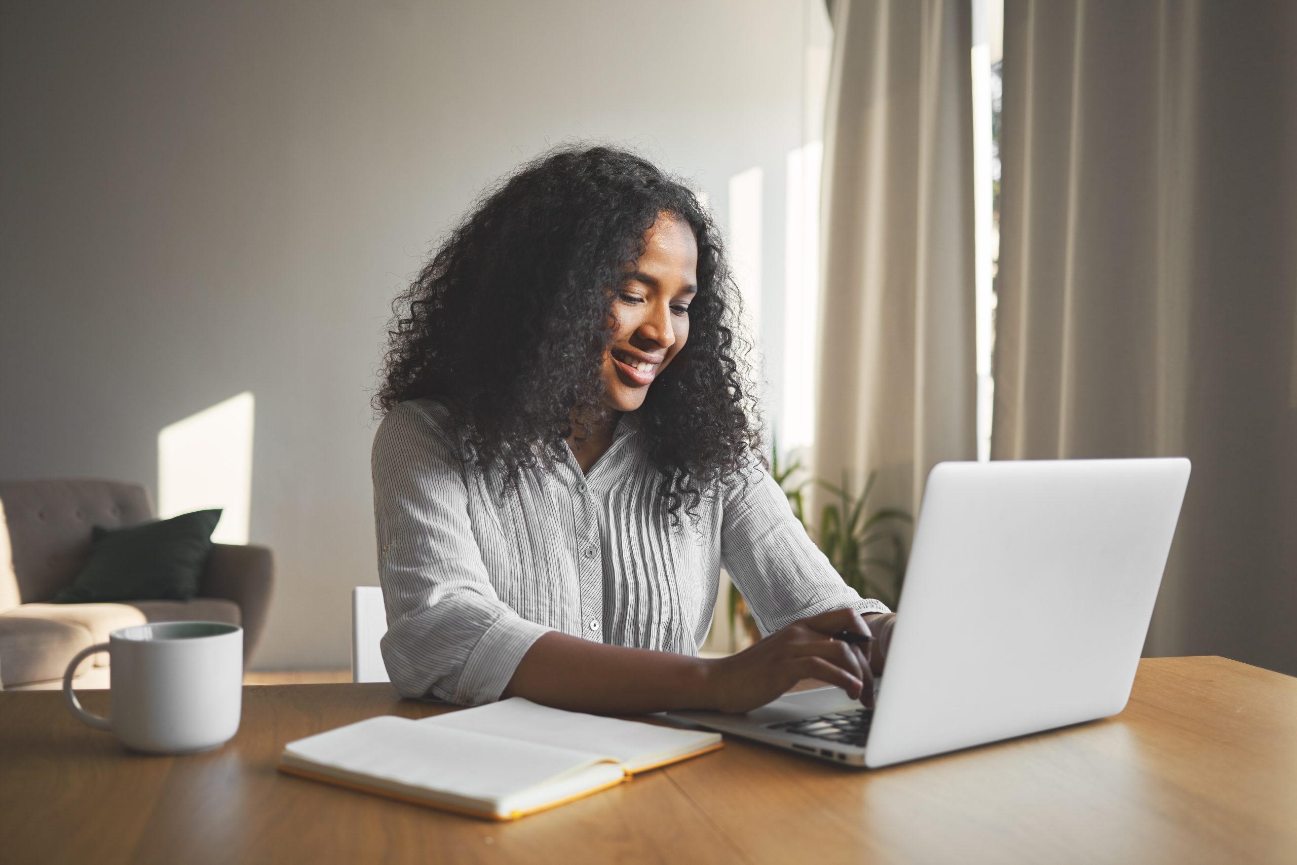 young dark skinned female blogger keyboarding on generic laptop