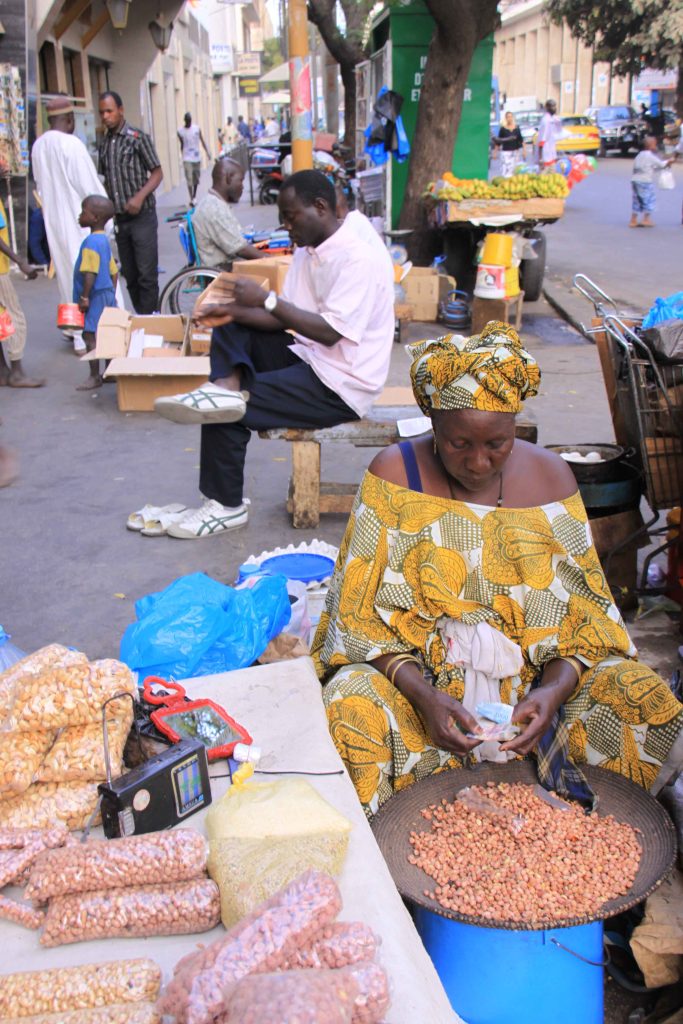Woman selling peanuts in bright yellow clothing.
