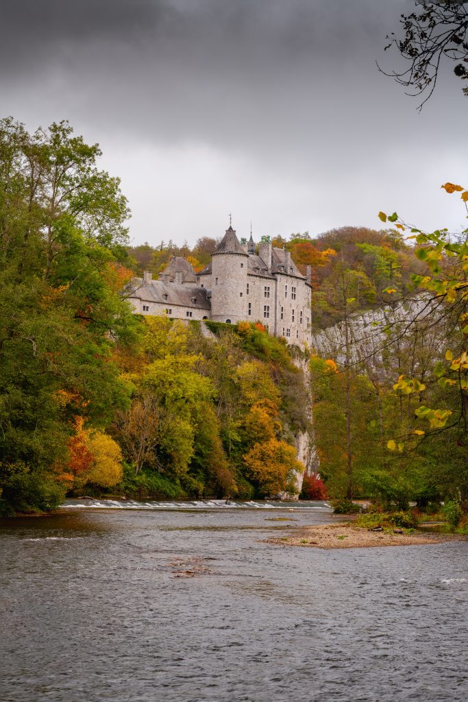 Castle on hillside at the edge of a river with trees and fall foilage.