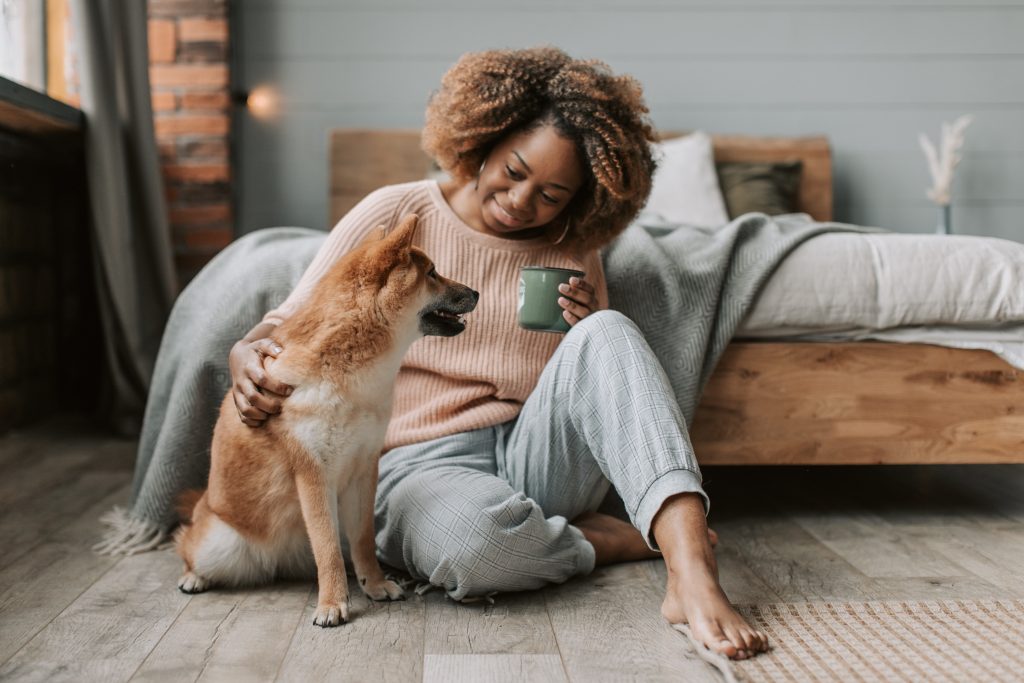 Woman sitting on wooden floor drinking coffee looking at her dog