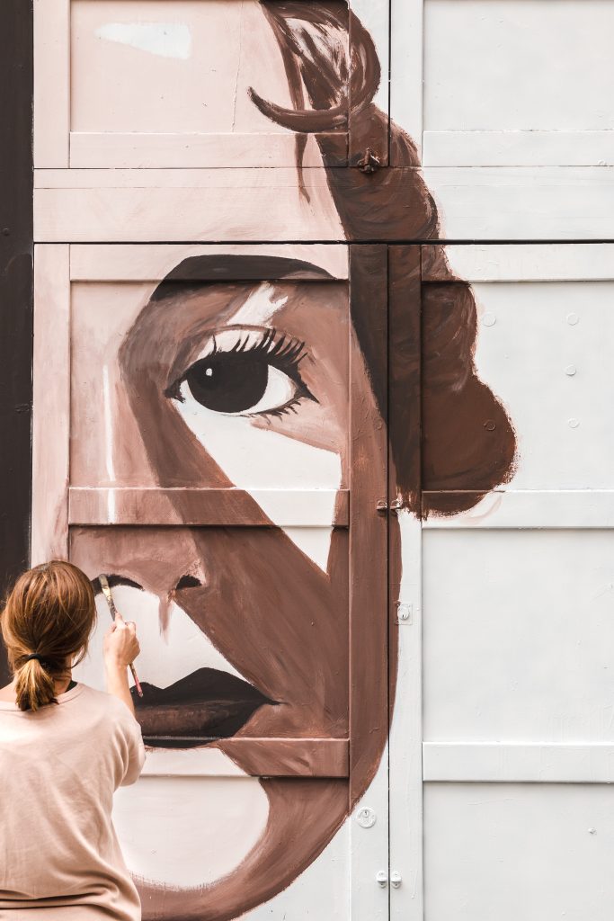 Woman painting a female portrait on large garage