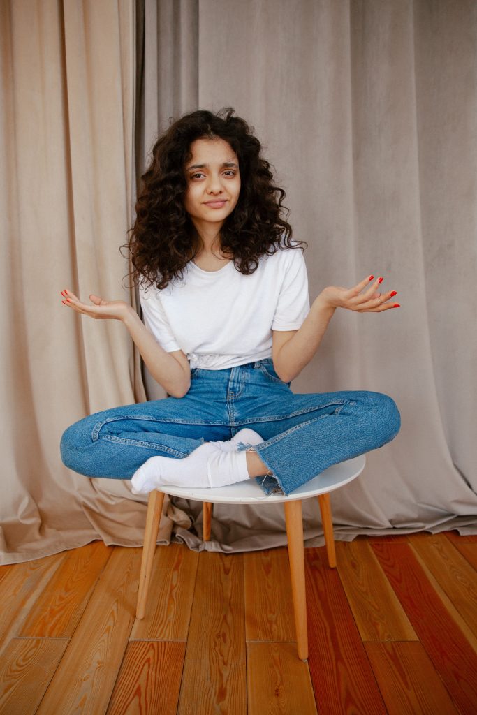 Person sitting on stool with hands up in a questioning gesture