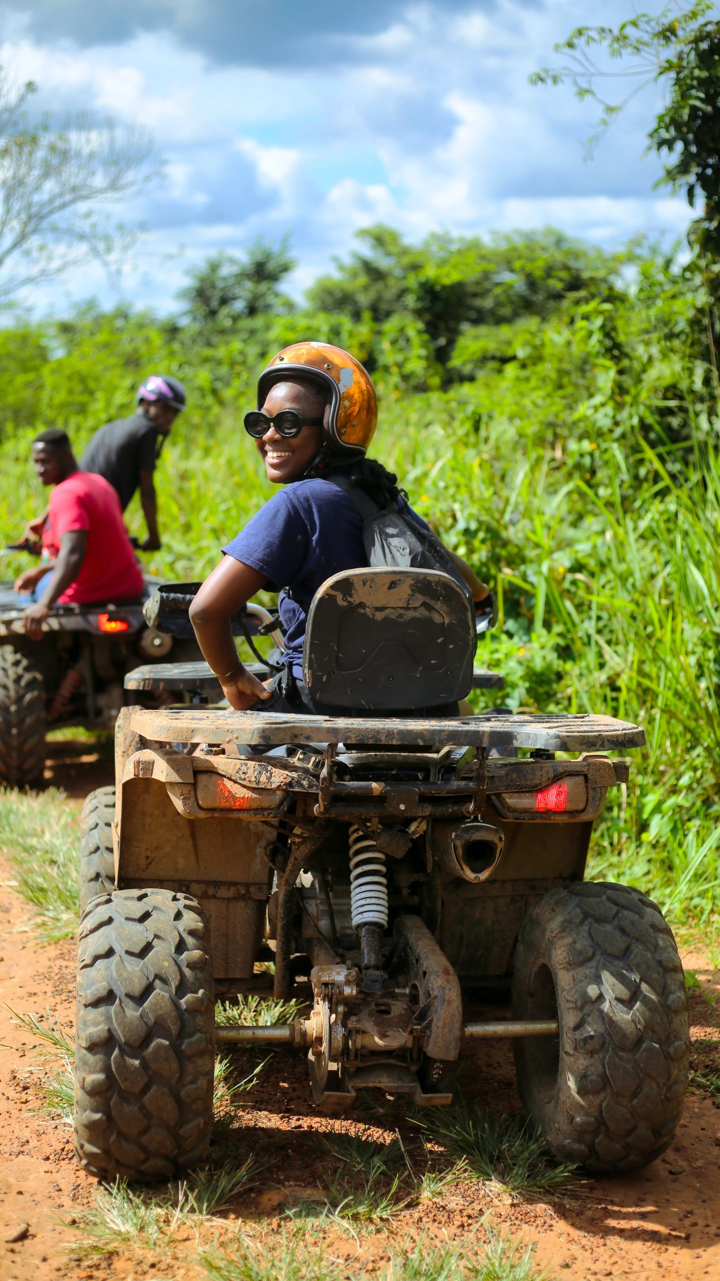 Person riding a four-wheeler in a jungle setting looking back at the camera smiling