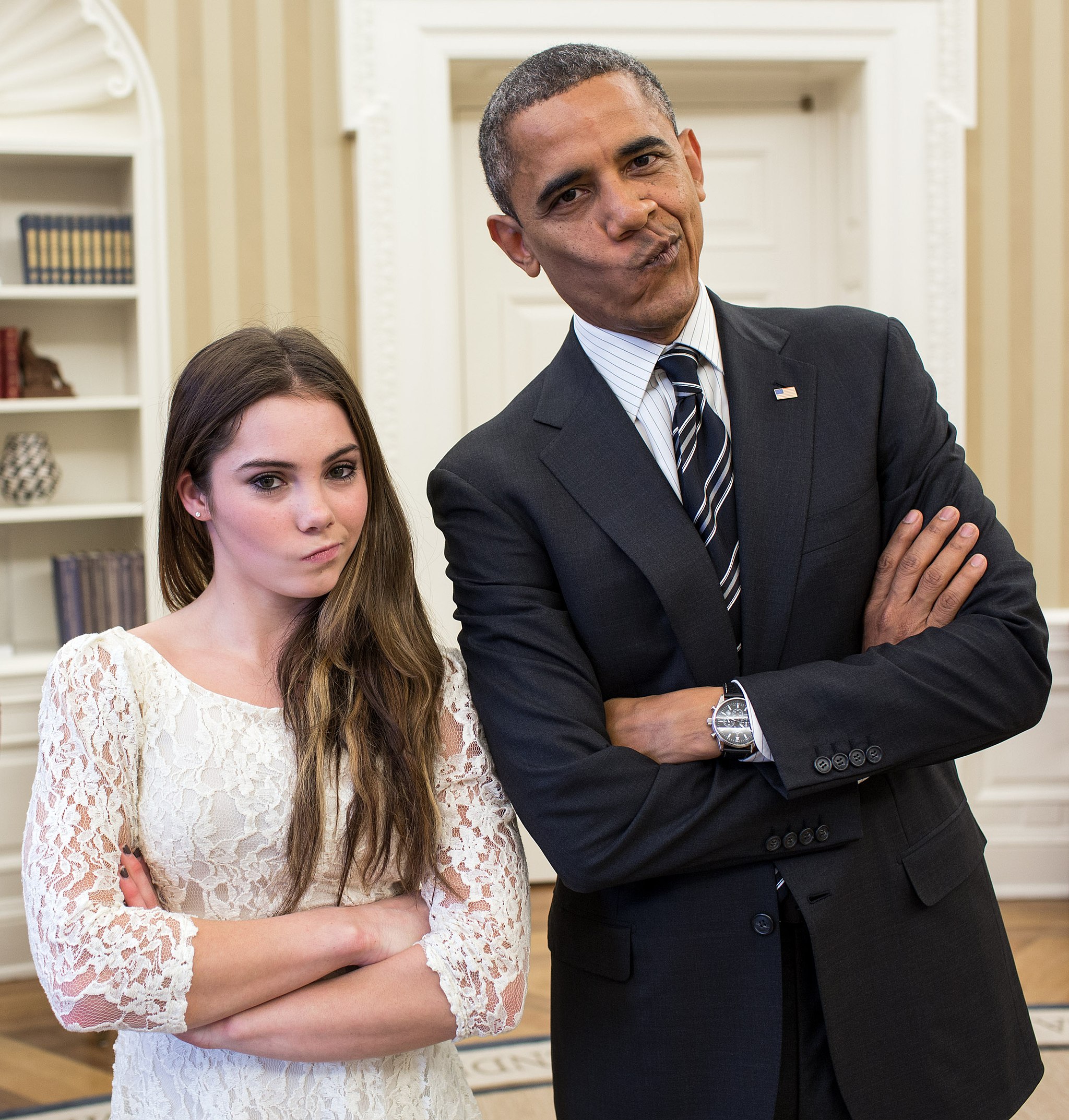 President Obama standing next to a young white woman. Both have their arms folding and a silly pout on their faces. President Obama is slightly leaning toward the young woman.