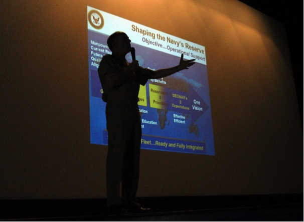 Person standing in front of a PowerPoint presentation with a microphone in their hand
