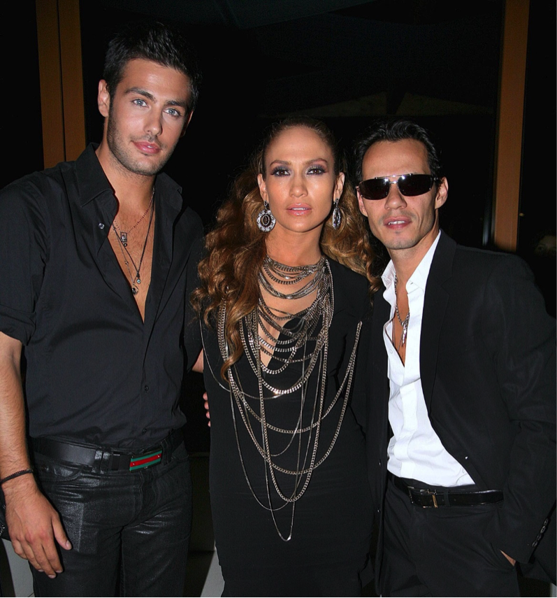 Three people dressed in black evening wear. Two males on each side of one female. One male wears sunglasses.