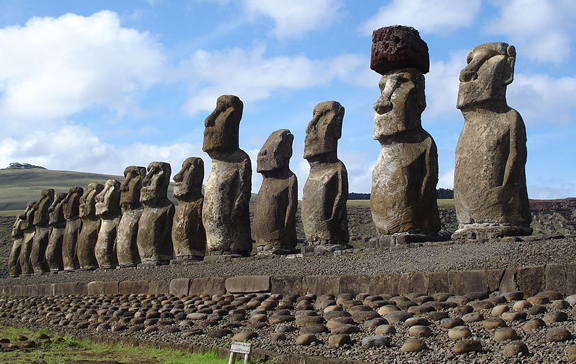 Row of large stone statues with large faces in front of a blue sky
