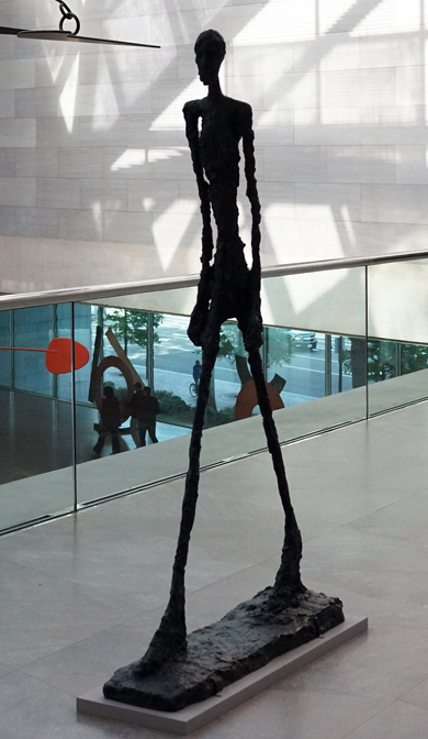 Tall stone statue of man with stick-like arms and legs