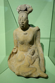 Stone figure kneeling with a child laying on lap and a large headdress