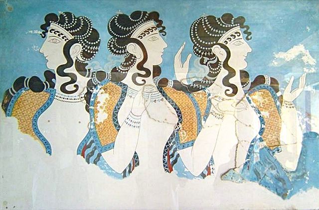Three pale women wearing golden sleeves with long, dark, curly hair wrapped in beads