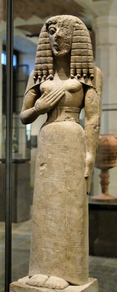 Stone woman with long hair and a hand on her ches