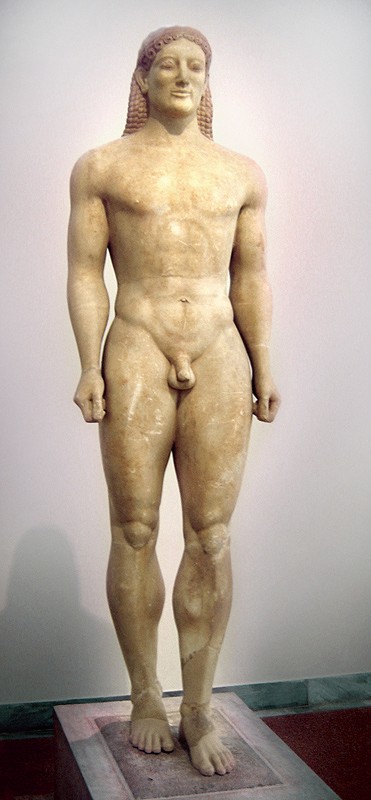 Stone statue of a very muscular naked man with long hair and one foot forward