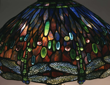 Lampshade made of many colored flecks of glass with upside down dragon flies on the bottom