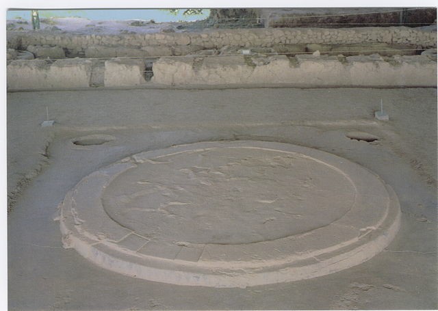 Large Round stone platform raised from the ground in front of small stone walls