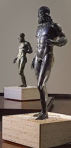 Two dark male statues with one arm bent and with long hair