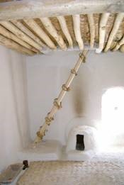 Wooden ladder leading to a log ceiling over a white stone room