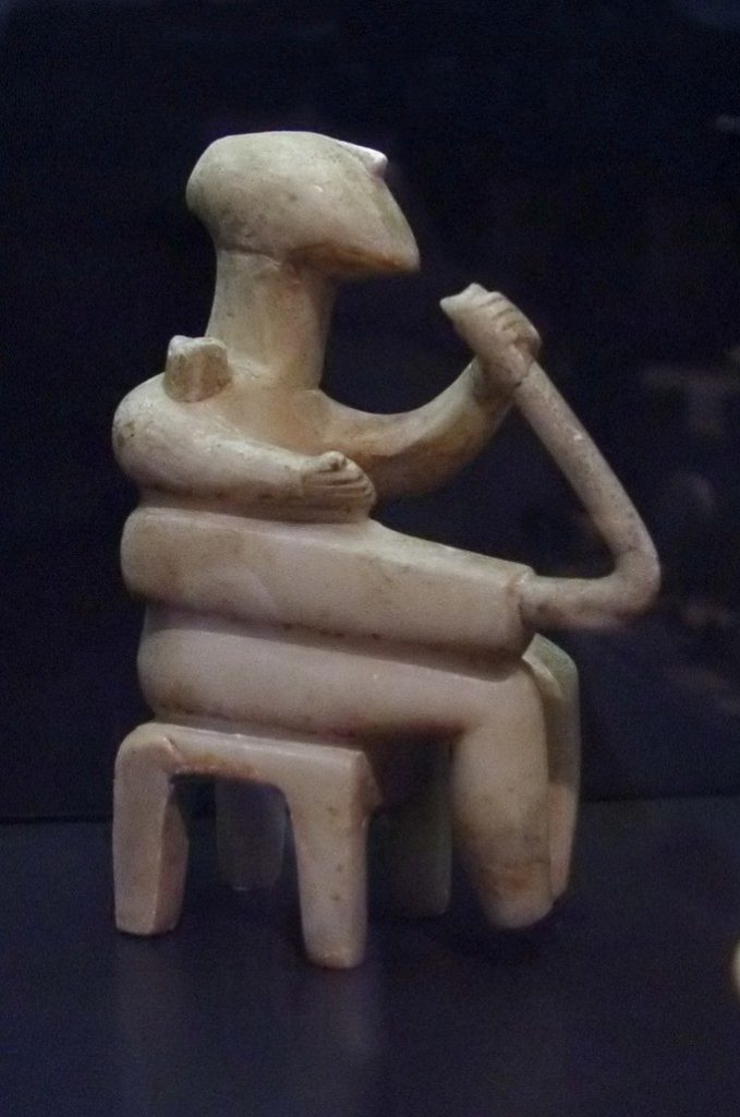 Faceless stone figure seated playing an instrument