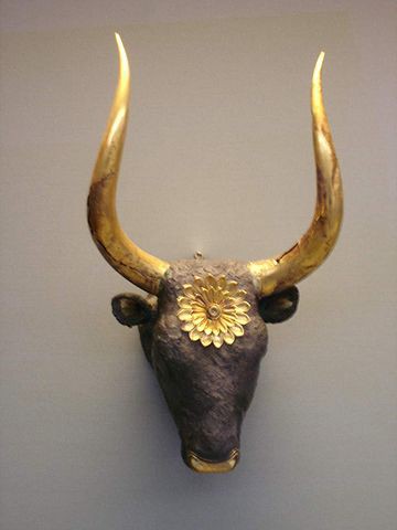 Dark head of a bull with long golden horns and golden flower on forehead