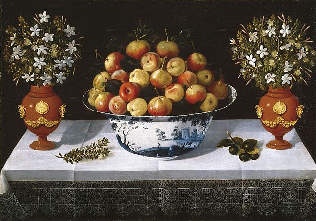 Bowl of apples an dplums on a table between two vases with white flowers