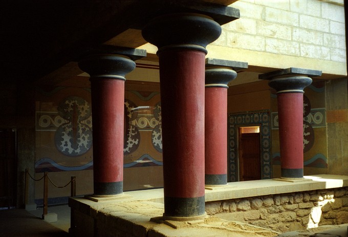 Four red pillars forming the corner of a balcony in front of painted wall and doorway