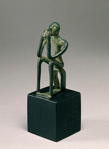 Greenish stone man seated on a cube with his elbows on his knees and hands on his face