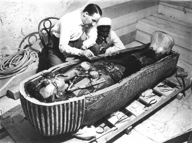 Two men kneeling over a coffin with a mummy in it