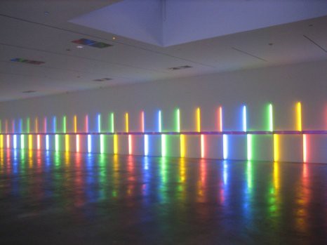 Bright colored lights in blue, green, red, and yellow lining the wall of an empty room