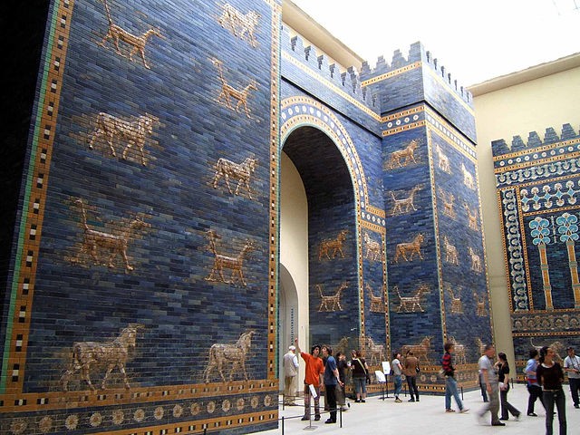 A crowd of people examining a large gateway made of blue stone carved with animals