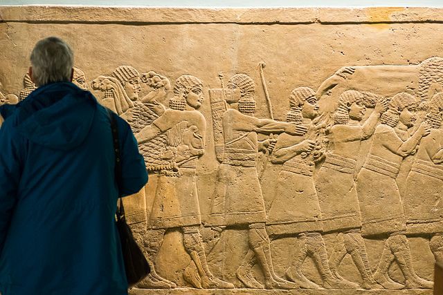 Man looking at a carving of Assyrian soldiers carrying a dead lion