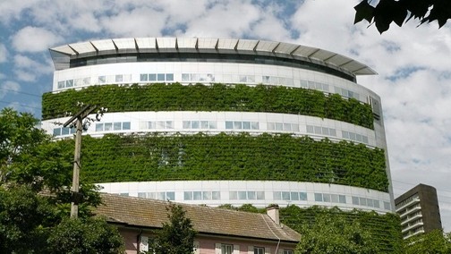 Rounded building with many windows interspersed with green plants