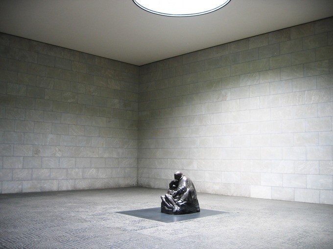 Stone figure of a woman clutching a child in a large empty room