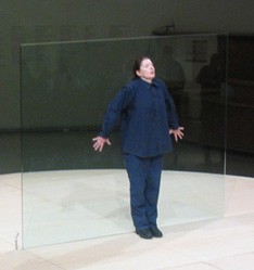A woman in blue standing with her hands against a wall of glass behind her
