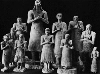 Many stone figures with their hands clasped standing in the dark