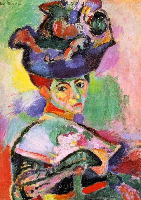A woman with a large hat seated before a colorful background