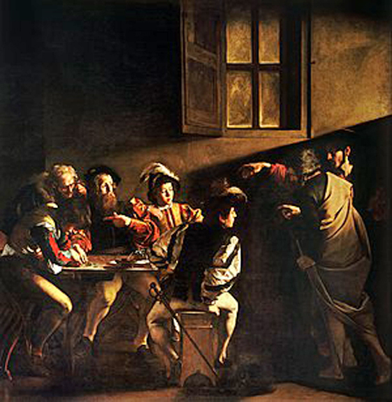 A group of men seated around a table and a man standing beside point to one of them