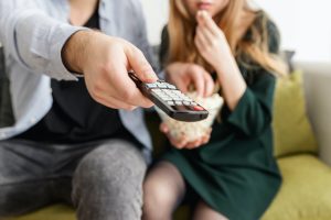 Two people pointing a remote and eating popcorn