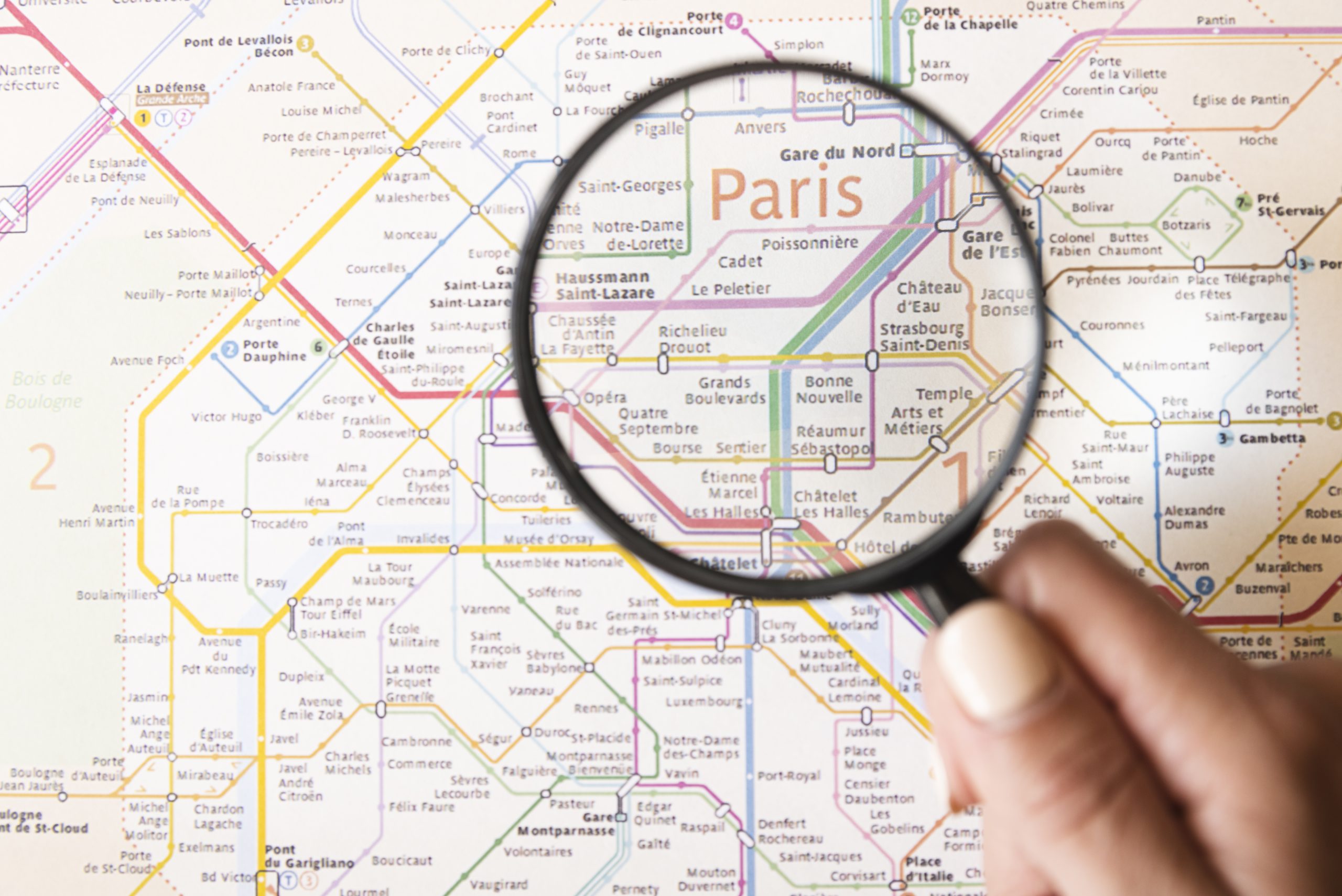 Someone holds a magnifying glass over the word "Paris" on a map of the Paris metro system