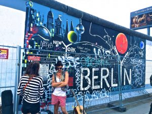 Picture of two women standing in front of a painted portion of the Berlin Wall.