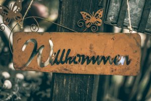Picture of a brown metal Willkommen sign hanging from a wooden post.