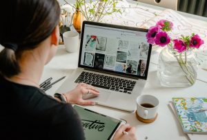 Photo of a woman at a computer, coffee and flowers.