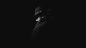 Silhouette of a man, dressed in black, in a fedora.