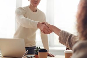 Photo of a man, at a desk with a computer, shaking hands with a woman.